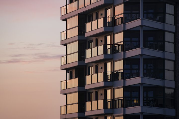 A modern apartment building with balconies against a pale pink evening sky