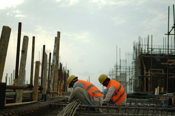 Two construction workers in hard hats and orange safety vests working on a building site