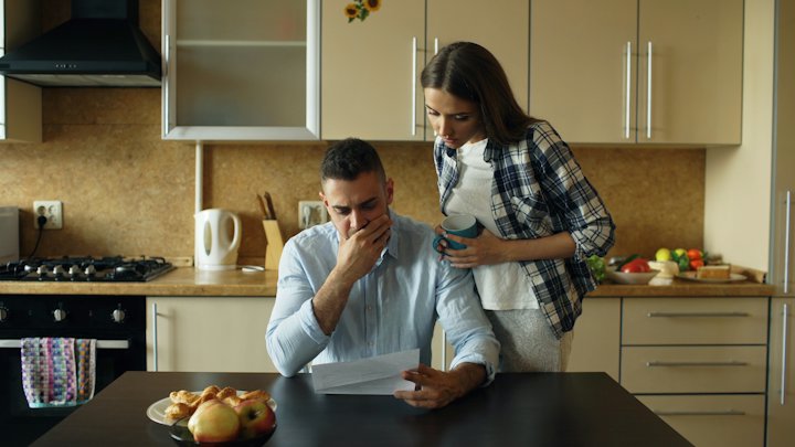 A man and a woman looking over a paper together at a kitchen table