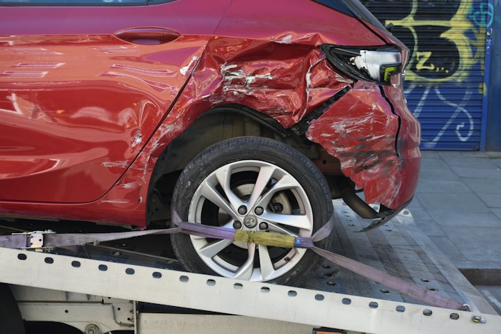 A red car with a crushed front corner strapped onto a flatbed tow truck