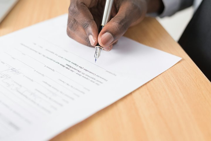 A hand filling in a printed form with a pen on a wooden desk