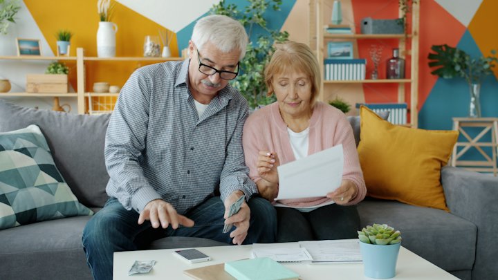 An older couple sitting on a sofa, reading through papers together