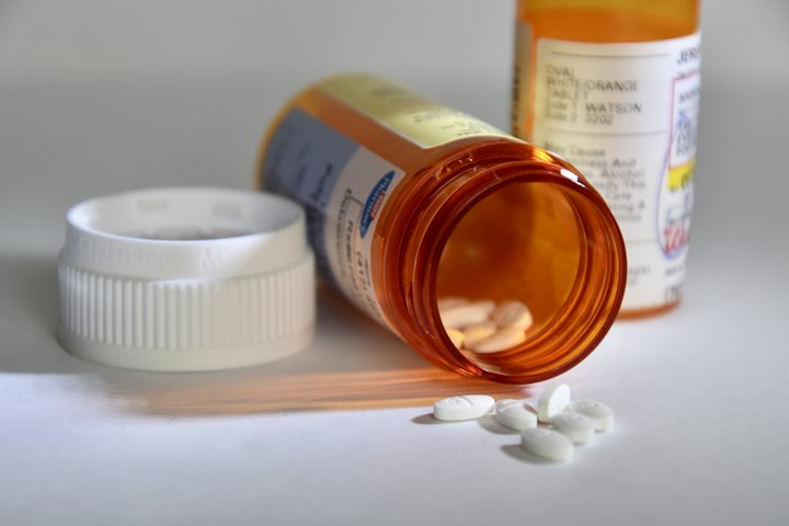 An orange prescription bottle lying on its side with white tablets spilled beside the cap