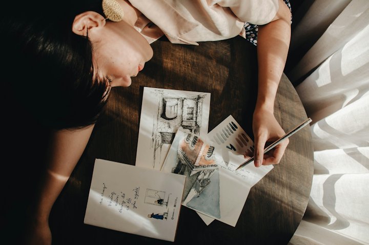 Seen from above, a person writing notes next to printed photos and papers on a table